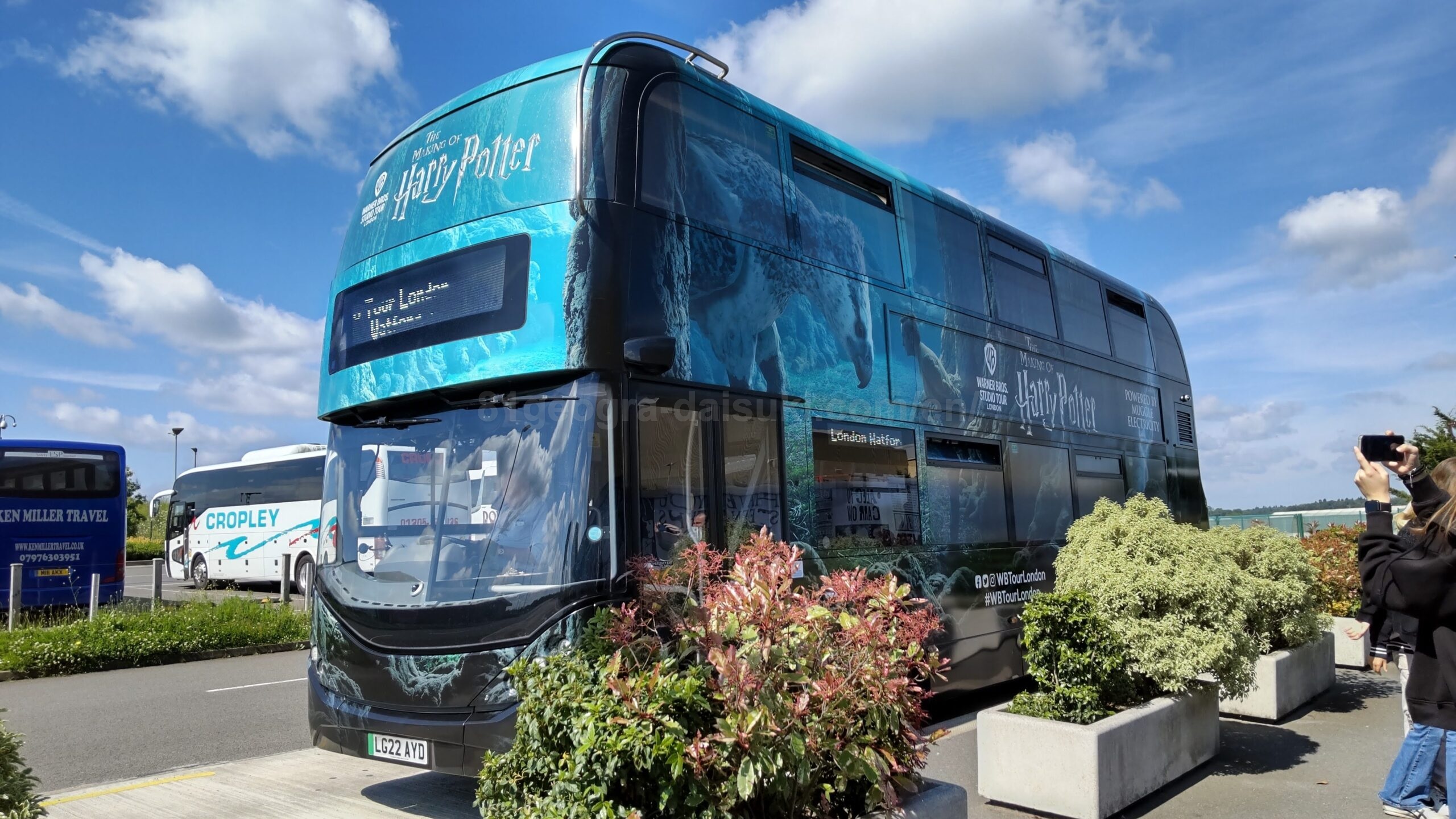 Harry Potter Studio Tour shuttle bus in London decorated with magical artwork under a bright blue sky.