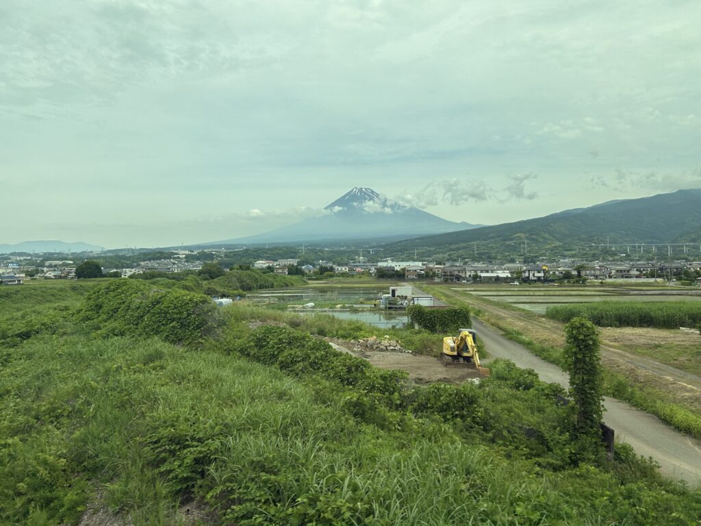 Mount Fuji above a blanket of clouds with rice fields and Japanese countryside seen from a Shinkansen E seat.